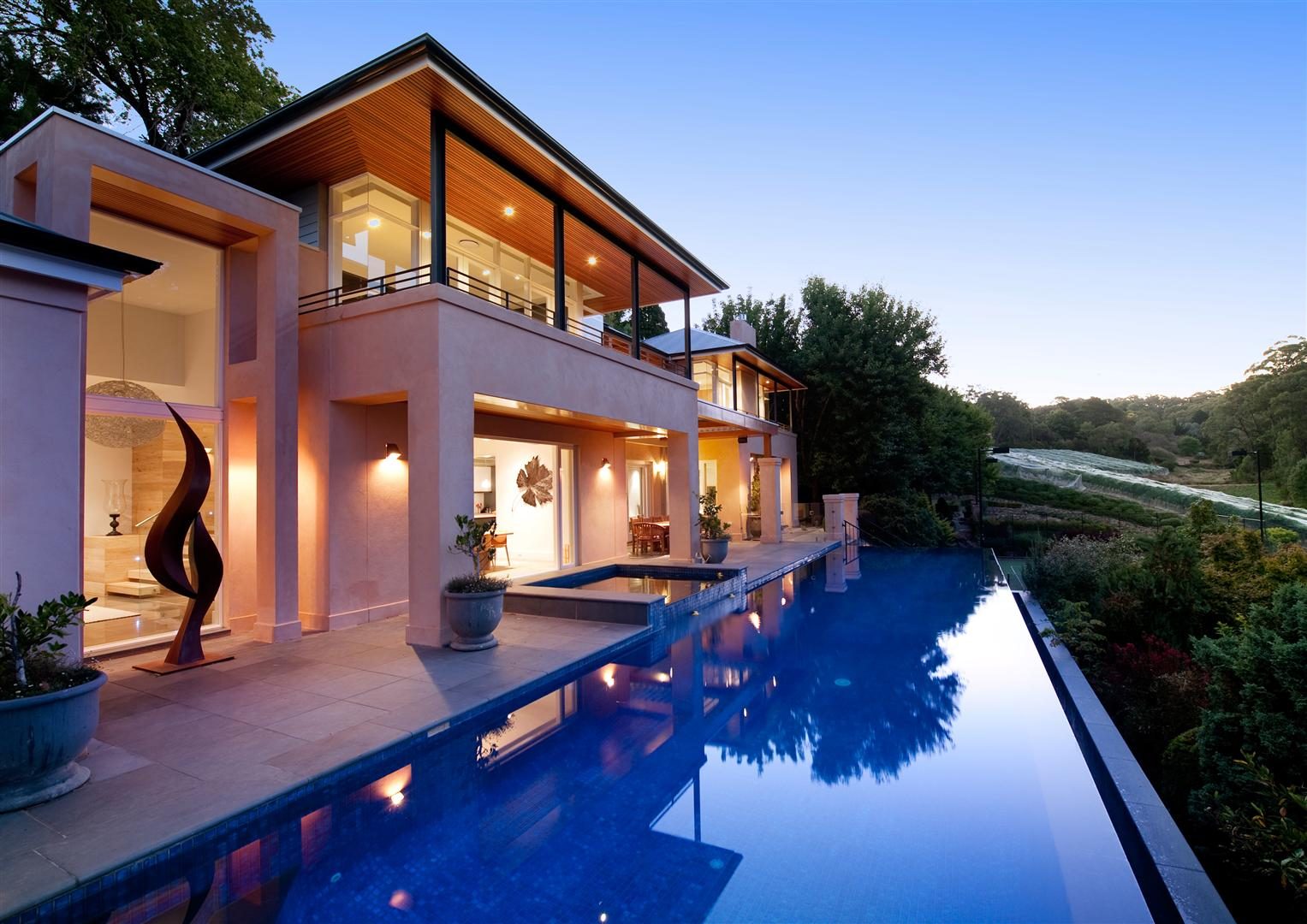 Aldgate Residence at dusk from the pool — the lit house reflected in an infinity pool, glass and stone across multiple levels