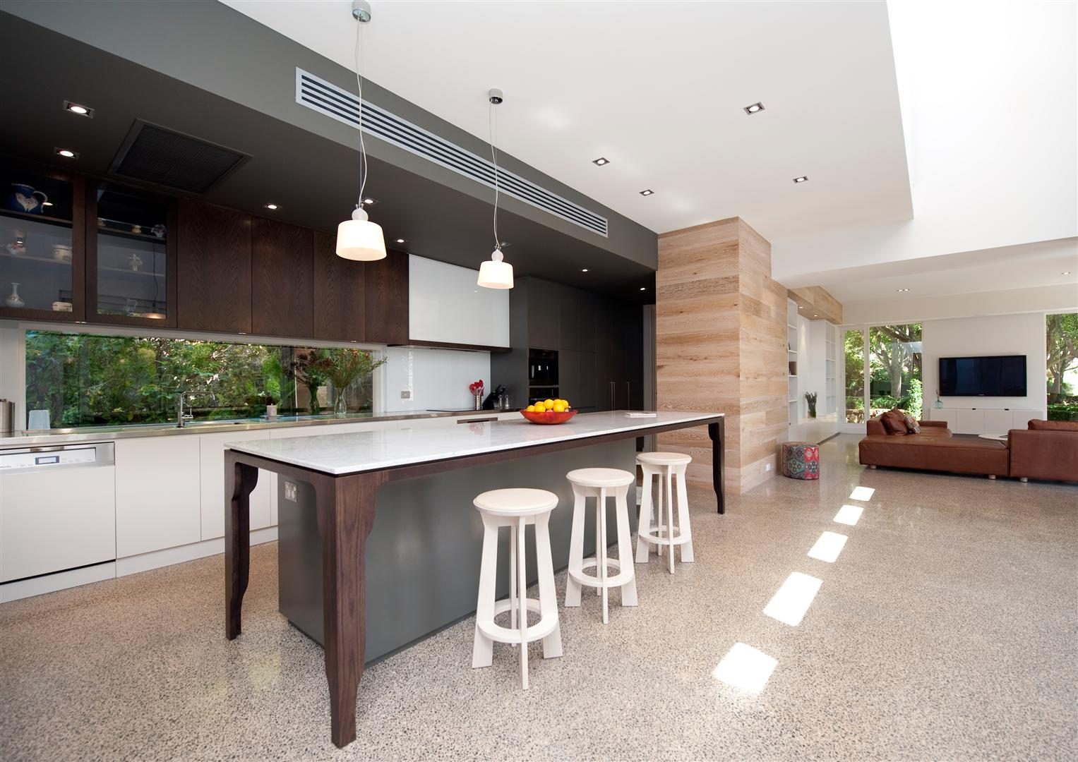 Kitchen and living — a long island bench with stools on a terrazzo floor, timber joinery, opening to the living area and garden