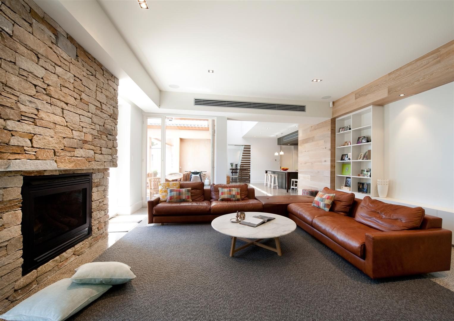 Living room — a stacked-stone fireplace wall, leather sofas and built-in shelving, opening to the garden